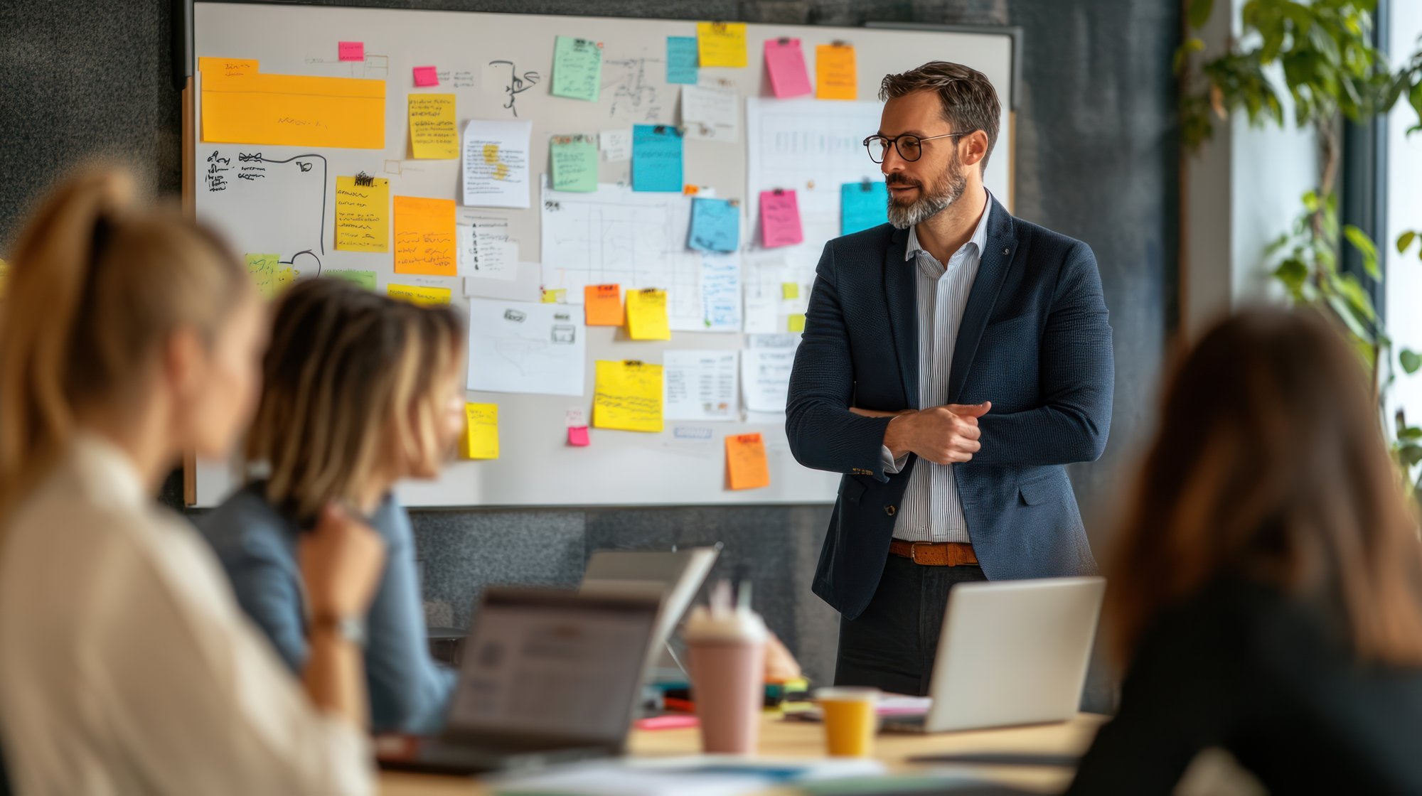 AI generated/adapted image: Ein Mann hält eine Präsentation vor einer Tafel mit Notizen.  Drei Frauen sehen den Vortrag an.